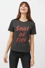 Remera de algodón negra de manga corta y cuello redondo, con estampa frontal que incluye letras rojas y gráficos en tonos dorados.