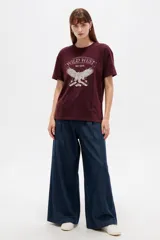 Remera bordó de manga corta y cuello redondo, con diseño holgado y estampado frontal de águila con la inscripción 'Wild West'.