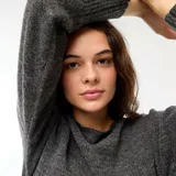 Sweater de punto gris oscuro, con escote Bardot (hombros descubiertos), manga larga y puño y ruedo acanalados. El calce es corto y holgado.