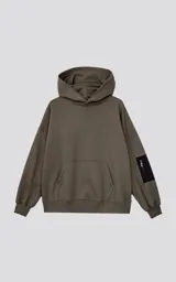 Hoodie oversize color verde militar, confeccionado en algodón rústico. Presenta capucha forrada, bolsillo frontal tipo canguro y un bolsillo adicional con cierre en la manga izquierda, con detalles en microfibra negra.