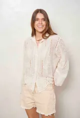 Camisa blanca de manga larga con bordados florales y detalles de ojales, cuello camisero y cierre frontal con botones ocultos.