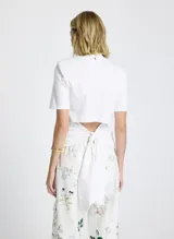 Remera blanca de tejido de punto, corte recto, cuello redondo, manga corta y cierre de lazo en la espalda.