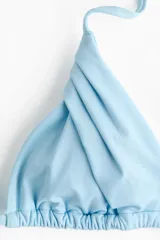 Top de bikini celeste con diseño triangular, copas plisadas y tiras finas para atar en el cuello y la espalda.