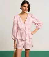 Blusa de tricolina con estampado de rayas verticales en color blanco y rosado. Presenta cuello en V, cierre frontal con botones, mangas 3/4 abullonadas y un lazo ajustable en la cintura.