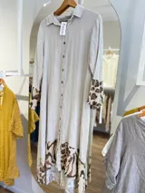 Vestido camisero largo de lino color beige con botones frontales, cuello camisero y mangas largas con puños. Presenta estampado animal print en mangas y ruedo.