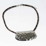 Collar con tira de cuero sintético con estampado animal print y dije plateado con textura irregular.