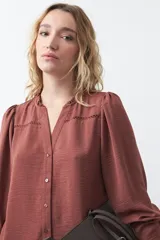 Camisa negra de corte clásico con escote en V, botones frontales y mangas largas con puños. Presenta detalles de recortes calados en la zona de los hombros.