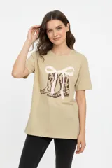 Remera de algodón color beige, de manga corta, cuello redondo a la base y corte holgado. Cuenta con un estampado frontal de botas estilo texanas con un moño en tonos marrones y rosados.