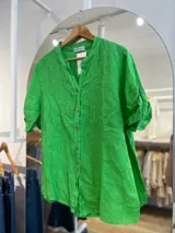 Camisa de lino color verde con cuello mao y cierre frontal de botones. Posee mangas cortas con detalle de presilla y botón para ajustar el largo, y un diseño de calce holgado con el ruedo posterior levemente más largo.