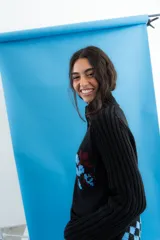 Cardigan de punto color marrón con cierre frontal, cuello alto y bolsillos aplicados. Presenta diseño tejido localizado con detalles en violeta y negro en el pecho.