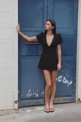 Vestido mini negro con escote en V amplio, mangas cortas abullonadas y detalle de lazo en el delantero. Cuenta con cierre de cremallera oculta en la espalda.