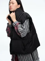 Chaleco puffer de corte holgado y diseño acolchado, con cuello alto, cierre frontal oculto y bolsillos laterales. Ideal para superponer sobre otras prendas.