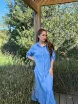 Vestido camisero largo de lino blanco, con cuello camisero, manga corta enrollada y cierre frontal de botones de nácar. Presenta aberturas laterales en el bajo.