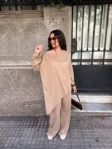 Buzo oversize gris melange de punto fino, con escote redondo amplio que se puede usar caído sobre un hombro, mangas largas amplias y diseño asimétrico más largo en la espalda.