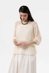 Sweater beige de punto abierto y liviano, con escote redondo, mangas largas y silueta amplia. Presenta detalle de broderie en el ruedo.