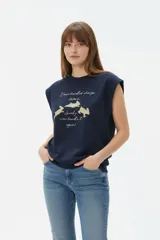 Musculosa color crudo con estampado frontal de paisaje montañoso y texto "EXPLORING Outlands", corte holgado y aberturas laterales en el ruedo.
