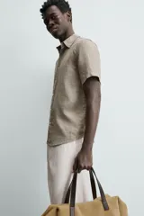 Camisa de lino color beige de corte relajado, con cuello solapa, manga corta y cierre frontal con botones.