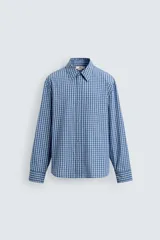 Camisa de manga larga con cuello solapa y bolsillo plastrón en el pecho. Presenta un estampado de cuadros pequeños en tonos azul y blanco. Cierre frontal con botones a presión.