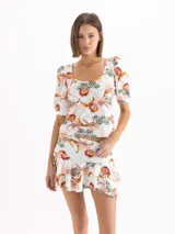 Remera blanca de punto con estampado full print colorido y textura suave, escote redondo profundo, mangas cortas con frunces y hombreras en la copa con puños ajustados, y corte al cuerpo.
