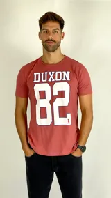Remera de algodón color coral con estampa frontal que incluye el texto DUXON y el número 82 en color blanco con bordes azules.