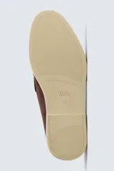 Mocasín casual de hombre, color marrón oscuro (bordó), fabricado en piel con acabado serraje (gamuza). Presenta un detalle de antifaz en el empeine y suela a contraste de color beige claro.