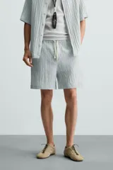 Bermuda negra de corte regular, confeccionada en tejido jacquard con efecto arrugado. Presenta cintura elástica ajustable con cordón blanco, bolsillos laterales y bolsillos traseros de vivo.