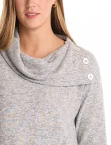 Buzo de calce suelto confeccionado en tejido suave melange color gris. Presenta cuello volcado con botones decorativos en el hombro izquierdo, mangas largas con hombros caídos y ruedo asimétrico con terminación en punta.