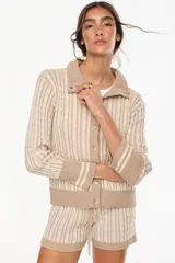 Cardigan de punto con patrón trenzado, color crudo y visón, con cuello solapa, cierre frontal de botones y mangas largas con puños elásticos rayados.