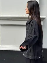 Campera clásica de jean negra con cuello camisero, bolsillos frontales y detalles de brillos plateados.