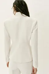 Blazer entallado color blanco de cuello sin solapa, manga larga con hombreras, falsos bolsillos delanteros de vivo y cierre frontal con un botón.