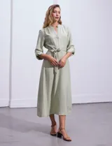 Vestido maxi color beige, con cuello mao y escote en V. Presenta mangas largas con presilla y botón para regular el largo, y un lazo ajustable en la cintura que marca la silueta.