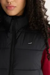 Chaleco acolchado negro con cuello alto y cierre frontal con cremallera. Tiene un logo pequeño de la marca en el pecho.