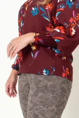 Blusa color borgoña con estampado de flores multicolores, escote en V con botones forrados, mangas largas con frunces en los puños y hombros.