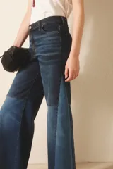 Jean de tiro alto con pierna palazzo, ajustado en cintura y caderas, con recortes a contratono en el lateral y a media pierna que generan un vuelo pronunciado. Confeccionado en tejido de elastano, incluye cierre y botón, y forrería de bolsillos estampada con el logo de la marca.