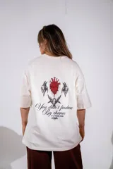 Remera de corte oversize color blanco, con cuello redondo y mangas cortas. Presenta un pequeño estampado gráfico central en el pecho con diseño de querubín con alas.