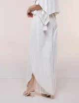 Pantalón palazzo cruzado color blanco con trama en hilo metalizado lurex, cintura elastizada con cordón ajustable con borlas y diseño de piernas anchas con bordes de puntilla y tajo profundo en el frente.
