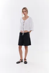Blusa de lino italiano color beige, de manga corta, con escote en V y cierre frontal mediante lazos o moños.