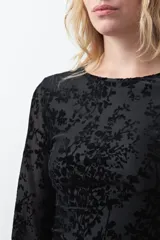 Vestido corto negro de silueta entallada, con mangas acampanadas y escote a la base. Presenta una superficie texturizada con estampado floral en relieve.