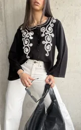Camisa negra de manga ancha con bordado floral blanco en el frente y cierre con botones.