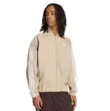 Campera Adidas Adicolor de color beige con cierre frontal y cuello bomber. Cuenta con las clásicas tres tiras blancas en las mangas y el logotipo del trébol bordado en el pecho.