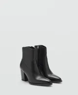 Botín de cuero vacuno color negro, con diseño de estilo western, punta fina y tacón bloque de 6,5 cm. Cuenta con cierre de cremallera lateral.