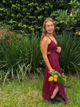 Vestido largo bordó de corte bajo el busto, con escote en V, top estilo triángulo, tirantes finos cruzados en la espalda y aberturas laterales (cut out). Cuenta con una falda larga con tajo y volados en el borde inferior.