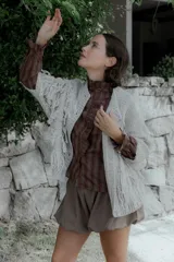 Saco de punto color crudo con diseño de flecos en el frente y mangas, cierre frontal con botones y cuello redondo.