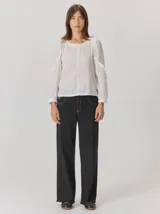 Camisa blanca de algodón con mangas largas abullonadas, detalle de volados en los hombros y puños elásticos. Presenta un diseño con cuello redondo y corte holgado.