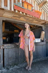 Camisa de corte holgado con estampado floral en tonos naranja y rosa, cuello clásico, manga corta y cierre frontal con botones de madera.