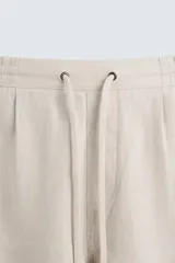 Bermuda de corte relajado color beige claro, confeccionada en lino. Presenta cintura elástica con cordón ajustable y bolsillos laterales y traseros.