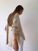 Buzo de tejido de punto color visón, con diseño holgado, cuello redondo, mangas largas con puños acanalados y costura central vertical visible. Presenta un ruedo asimétrico con aberturas laterales.