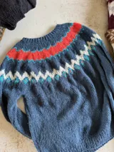Sweater de punto tejido a mano en mohair, con diseño de canesú estampado en tonos azul, rojo, blanco y turquesa. Presenta cuello redondo y mangas largas.