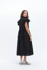 Vestido midi de lino blanco con diseño de broderie, cuello alto, cierre frontal con botones y volados decorativos en los hombros y el cuerpo.