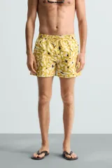Bañador de hombre de tejido técnico ripstop, color mostaza con estampado floral abstracto en blanco y negro. Presenta cintura elástica ajustable con cordón, bolsillos laterales y bolsillo trasero de plastrón.